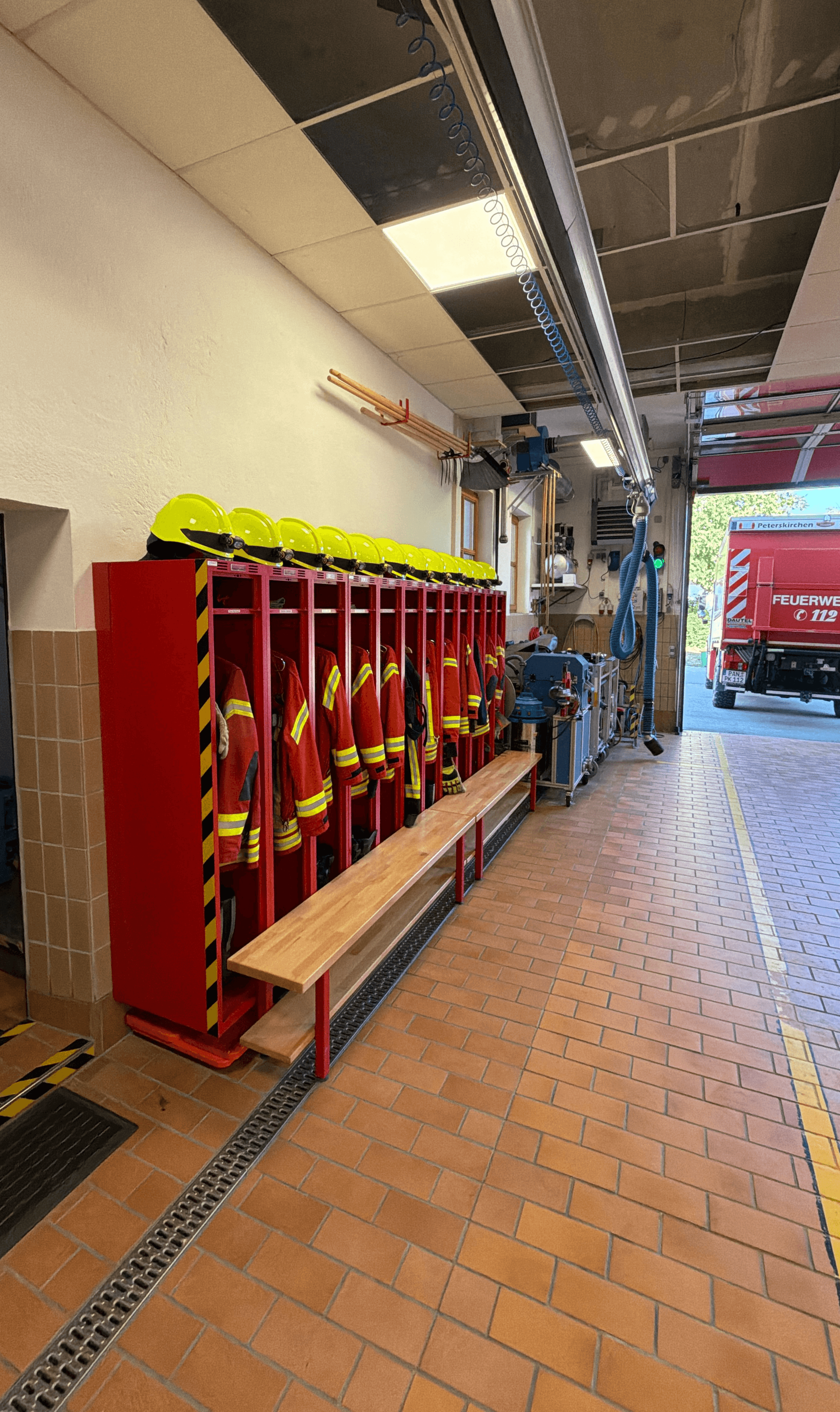 Spinde mit Einsatzkleidung der aktiven Mannschaft in der Fahrzeughalle des Feuerwehrhauses, im Hintergrund das geöffnete Sectionaltor